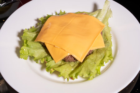 A low-carb lettuce-wrapped burger featuring a juicy patty topped with two melted slices of yellow cheese. The lettuce acts as a bun alternative, served on a white plate with a dark background.の写真素材
