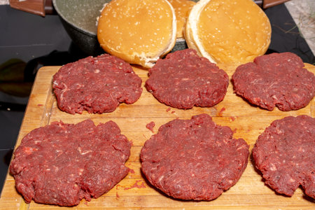 Six raw ground beef patties neatly placed on a wooden cutting board. The coarse-textured patties are fresh and ready for grilling or frying, capturing the essence of burger preparation.の写真素材