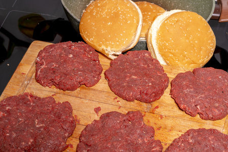 Six raw ground beef patties neatly placed on a wooden cutting board. The coarse-textured patties are fresh and ready for grilling or frying, capturing the essence of burger preparation.の写真素材