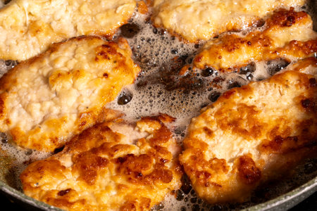 Golden-brown breaded chicken pieces sizzling in hot oil inside a pan. Crispy texture and bubbling...