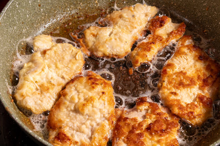 Golden brown breaded chicken pieces sizzle in a pan of hot oil, with bubbles forming around them. The crispy texture and rich color highlight the delicious frying process.の写真素材