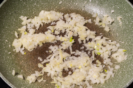 Diced white onions spread across the surface of a frying pan with a speckled green coating. The onions are in the early stages of sauteing, showcasing the cooking process.の写真素材