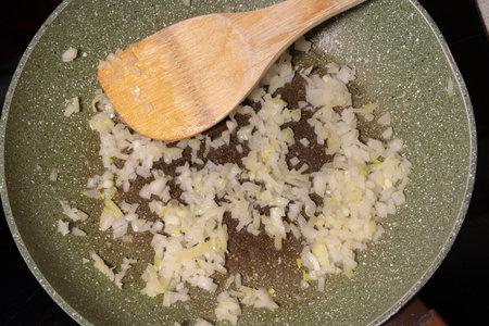 Diced onions sauteing in a pan, lightly cooked and turning translucent. A wooden spatula rests in the pan, showing the initial step in building flavors for recipes.の写真素材