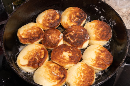 Golden-brown fried bread pieces sizzling in a cast iron skillet, glistening with oil. The rustic cooking process captures texture, warmth, and home-cooked simplicity on a stovetop.の写真素材