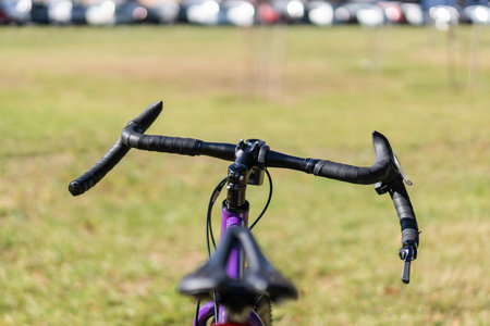 Front view of a road bike's handlebar and saddle, showing drop-style grips, integrated brake levers, and ergonomic cockpit design in an outdoor setting. Selective focus.の写真素材