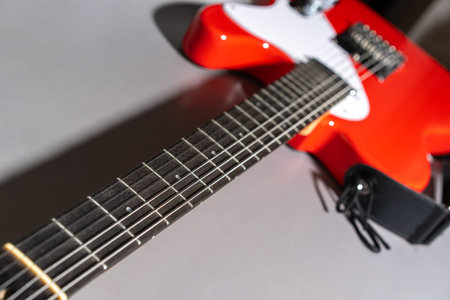 Close-up of a red electric guitar showing the fretboard with metal frets and dot inlays, strings...
