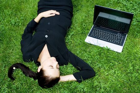 Businesswoman lying on grass with laptopの写真素材