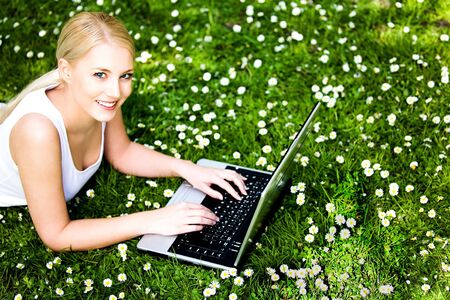 Woman laying on grass using laptopの写真素材