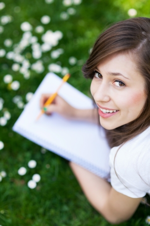 Girl lying on grass with workbookの写真素材