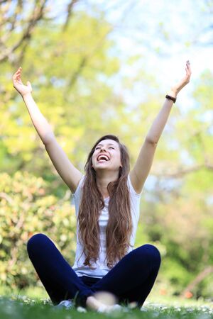 Excited woman sitting with arms raisedの写真素材