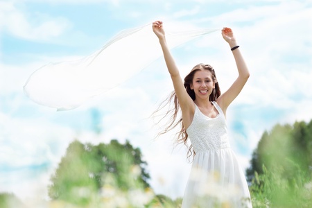 Young woman holding white scarf to windの写真素材