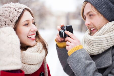 Young man taking photo of woman in winterの写真素材