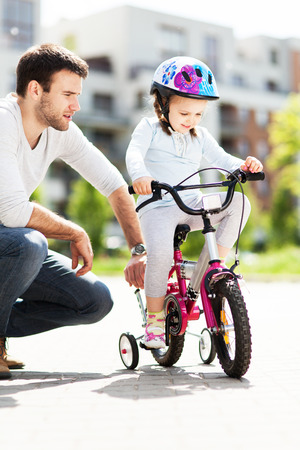 Girl learning to ride a bicycle with fatherの写真素材