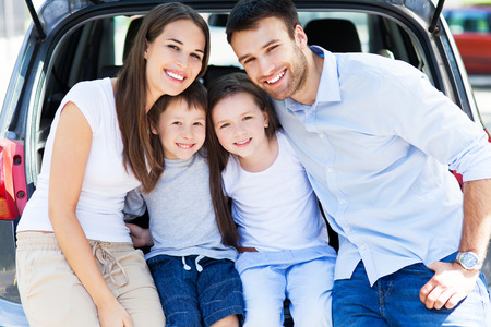 Happy family of four sitting in car trunk の写真素材