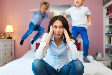 Mother with headache and children jumping on bedの写真素材