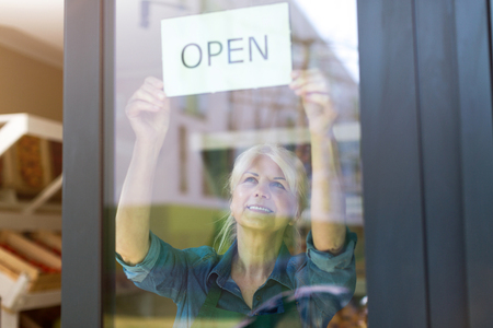 Senior woman holding an open sign in organic produce shop