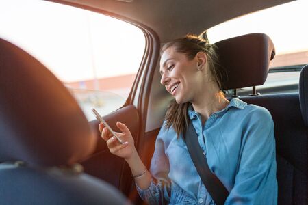Young woman with smartphone on the back seat of a car