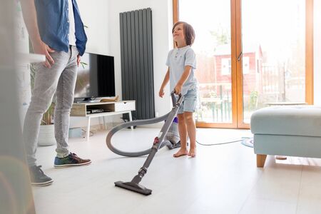 Boy vacuuming floor while father standing at homeの写真素材