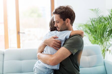 Father embracing son while sitting on sofa at homeの写真素材