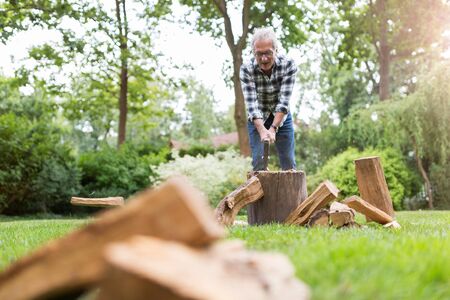 Senior man cutting logs, working in the garden (focus on ax)の写真素材