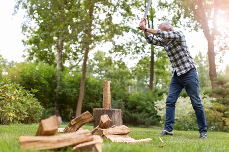 Senior man cutting logs, working in the garden (focus on ax)の写真素材