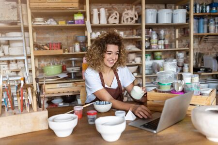 Woman pottery artist using laptop in art studio
