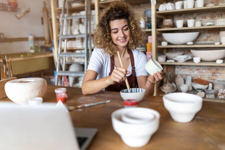 Craftswoman painting a bowl made of clay in art studioの写真素材
