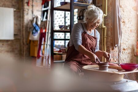 Hand made ceramics are formed by a mature woman on a potters wheel