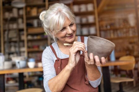 Senior woman pottery artist makes ceramics from clayの写真素材