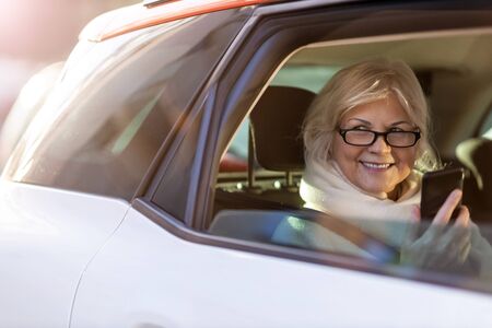 Senior woman with smartphone on the back seat of a carの写真素材