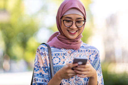 Portrait of confident young woman wearing hijab standing with mobile phone outdoorsの写真素材