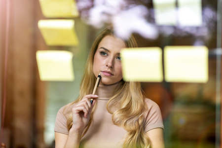 Young businesswoman brainstorming with notes on a glass wall in an officeの写真素材