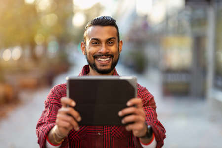 Smiling young man using tablet outdoors at urban setting