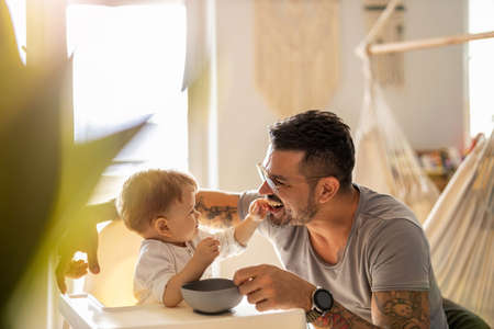 Single dad feeding his baby who is sat in a high chairの写真素材