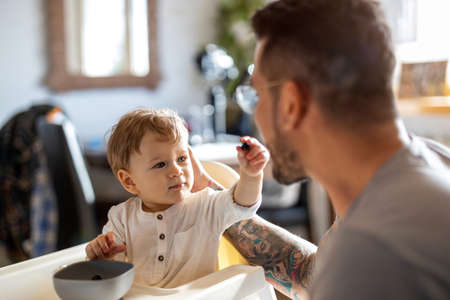 Single dad feeding his baby who is sat in a high chairの写真素材