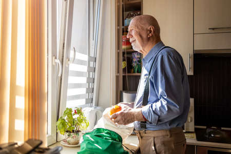 Senior man in kitchen at home looking out of windowの写真素材