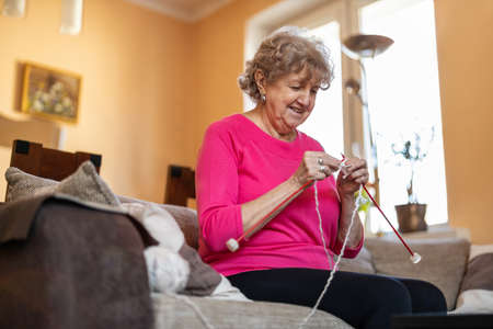 Senior woman sitting on sofa at home knitting