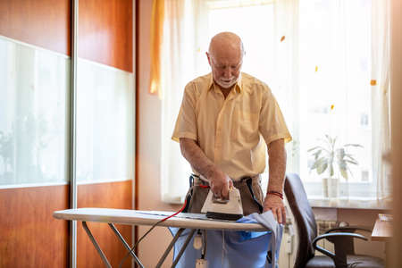 Senior man at home ironing his clothesの写真素材