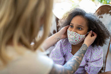 Mother putting protective face mask on daughter