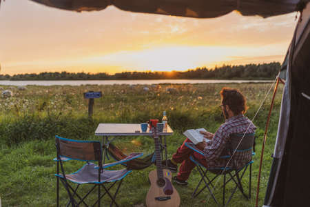 Man reading a book at a campsite. View from a tentの写真素材