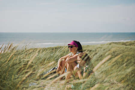 Mother and daughter sitting in the grass by the seaの写真素材