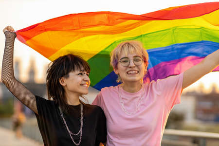Portrait of happy non binary couple waving rainbow flagの写真素材