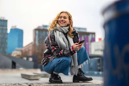 Smiling young woman in the city holding mobile phone