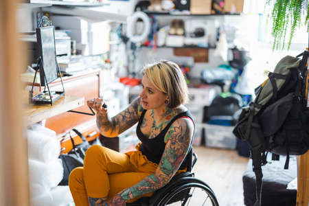 Portrait of an young tattooed woman in a wheelchair at homeの写真素材