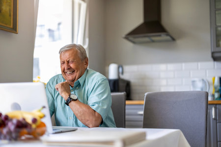Elderly man using laptop at kitchen tableの写真素材