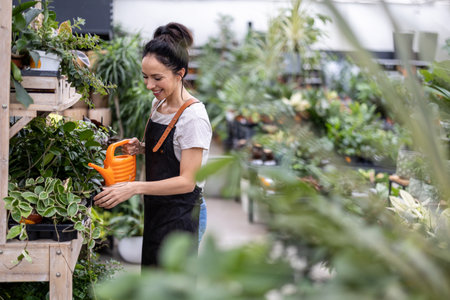 Woman working in greenhouse, watering flowersの写真素材