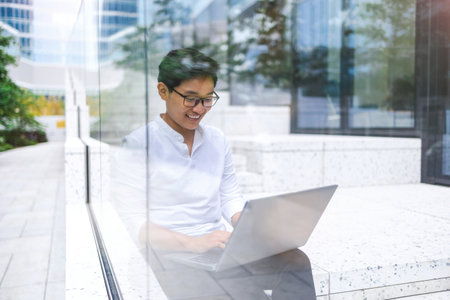 Young businessman sitting outdoors in the city working on laptop