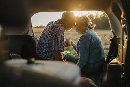 Happy senior couple sitting in car open trunk in the wildの写真素材
