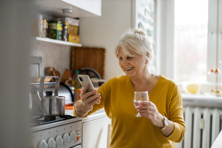 Mature woman using mobile phone while sitting in the kitchen at home