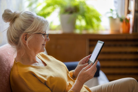 Senior woman using digital tablet while sitting on sofa in living room at homeの写真素材